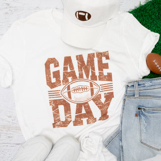 White T-shirt with brown "GAME DAY" and football graphic, white hat with football logo, denim shorts, and football decor.
