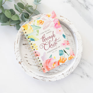 Spiral bound journal with watercolor floral print and I Can Do All Things Through Christ text on a white wooden tray