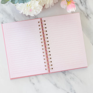 Open She is Brave spiral wire bound pink journal with lined pages on a marble surface