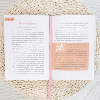 Open devotional book titled You Are Made for This Devotions to Uplift & Encourage Busy Moms resting on woven mat with pink ribbon bookmark