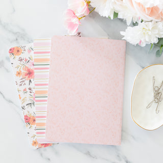 Three He Leads Me Beside Still Waters Psalm 23:2 blank notebooks with floral and striped covers on a marble surface