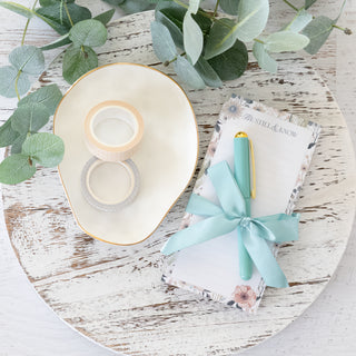 Be Still and Know floral notepad with teal pen and ribbon on a white wooden surface with washi tape