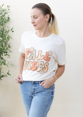 Woman wearing a cream Fall Vibes Retro Daisies graphic tee with blue jeans