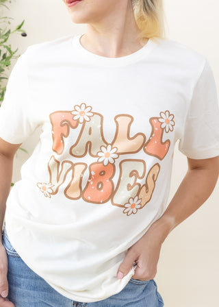 Cream color graphic tee with retro Fall Vibes text and daisy flower accents