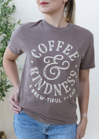 Person wearing a brown t-shirt with Coffee and Kindness A Brew-tiful Blend graphic