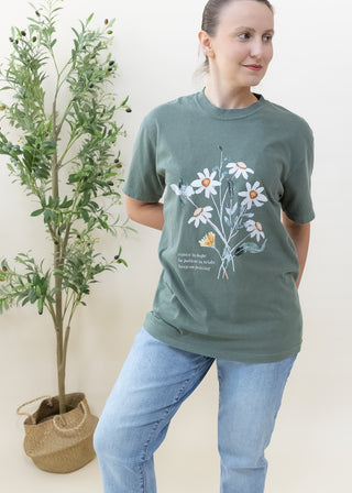 Woman wearing dark green Rejoice in Hope Be Patient in Trials Keep on Praying graphic tee with floral design