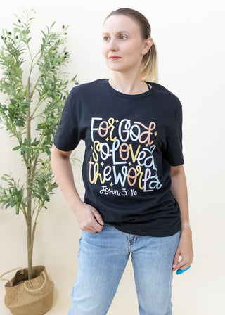 Woman wearing black For God So Loved the World graphic tee with colorful lettering and John 3:16 text