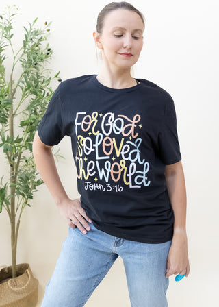 Woman wearing a black For God So Loved the World graphic tee with colorful lettering and John 3:16 text