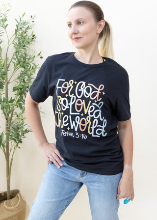 Woman wearing a black For God So Loved the World graphic tee with colorful lettering and John 3 16 text