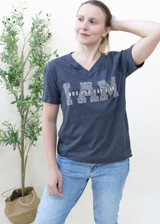 Woman wearing I Am Who You Say I Am graphic tee in heather black with blue jeans