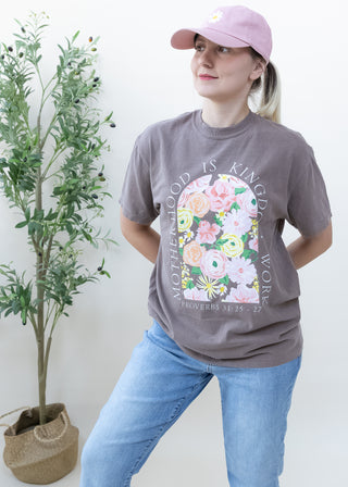 Person wearing light chocolate brown Motherhood Is Kingdom Work Proverbs 31:25-27 graphic tee with floral arch design