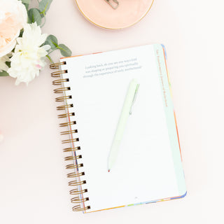 Open page of Moms Faith Journey journal with a pen and flowers on a desk