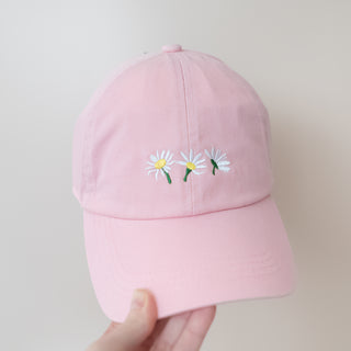 Three Summer White Flowers Pink Baseball Cap with embroidered daisies held against a neutral background