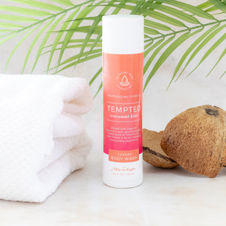 Mixologie Tempted Coconut Kiss luxury body wash bottle next to a white towel and coconut halves