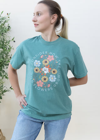 Woman wearing a teal Consider How the Wild Flowers Grow Luke 12:27-28 graphic t-shirt with floral design
