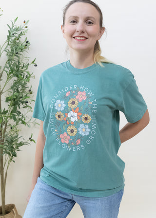 Woman wearing Consider How the Wild Flowers Grow Luke 12:27-28 graphic t-shirt in teal