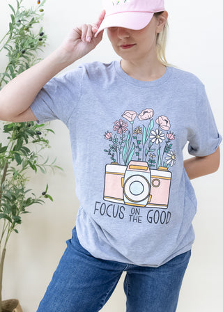 Grey t-shirt with a camera and flower graphic and the text Focus On The Good