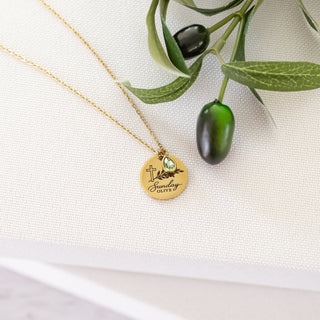 Gold necklace with Sunday Olive pendant and green gemstone, olive branch in background