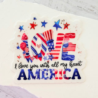 Sticker with 'I love you with all my heart America' text held by a hand against a natural background.
