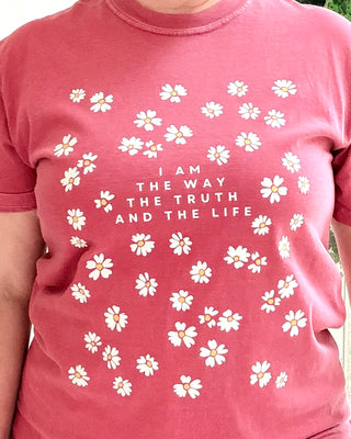 Pink t-shirt with white floral patterns and text on a person wearing it.