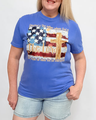 Person wearing a blue t-shirt with an American flag and cross design on a plain background