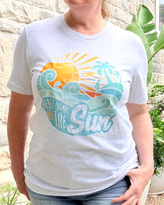 Person wearing a white t-shirt with a sun and wave design, standing outdoors.