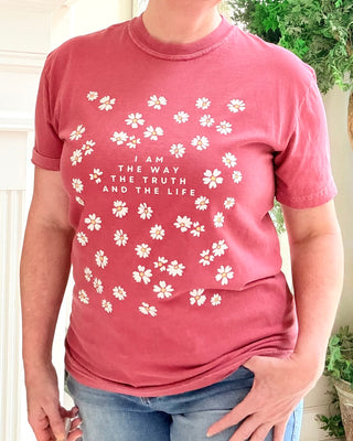 Person wearing a red t-shirt with white floral patterns and text.