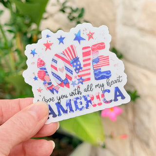 Sticker with 'I love you with all my heart America' text held by a hand against a natural background.