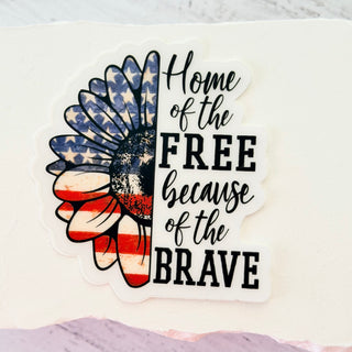 Sticker with American flag design and text 'Home of the Free because of the Brave' on a white background.