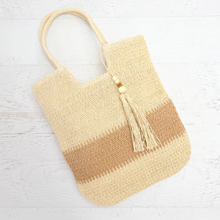 Beige woven handbag with a tassel on a light wooden surface