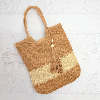 Brown woven tote bag with a tassel on a light wooden surface