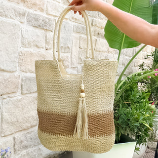 Woven handbag with a tassel held by a person against a stone wall and plant background