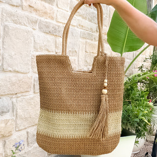 Woven tote bag with a tassel held by a person against a stone wall.
