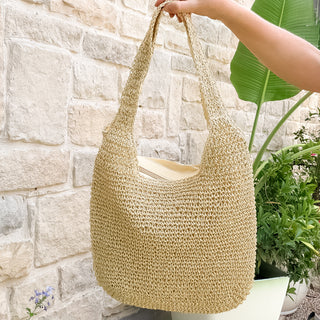 Woven straw bag held by a hand against a stone wall and plant background