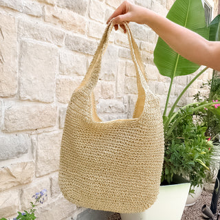 Woven straw bag held by a hand against a stone wall and plant background