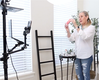 Woman holding a pink skincare product while recording a video with a smartphone on a tripod
